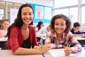 Portrait of teacher with elementary school girl at her desk